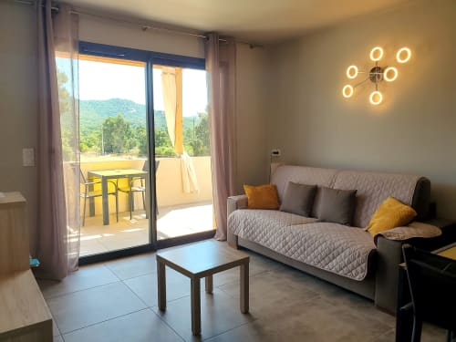 Modernes 1-Zimmer-Apartment in den Villas Lantana in Lecci mit grauem Sofa, gelben Akzenten und Bergblick vom Balkon