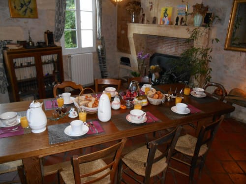 Salle à manger élégante avec table en bois dressée pour le petit-déjeuner au Sous Les Marronniers B&B, avec viennoiseries, jus et cheminée