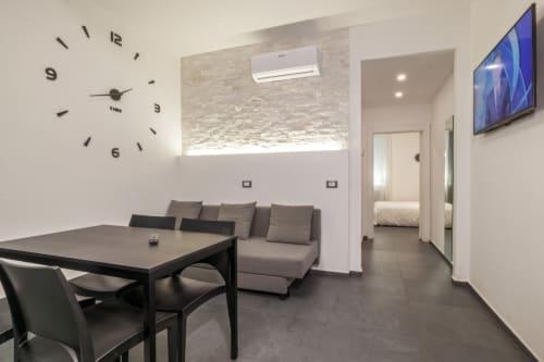 Moderno appartamento a Casa Mirko Arezzo con tavolo da pranzo, divano grigio, orologio da parete e TV
