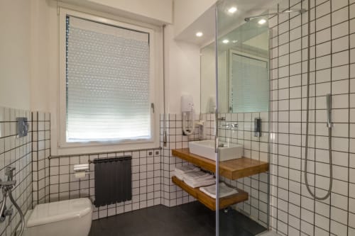 Bagno moderno dell'appartamento Casa Mirko ad Arezzo con box doccia, scaffali in legno e pareti piastrellate