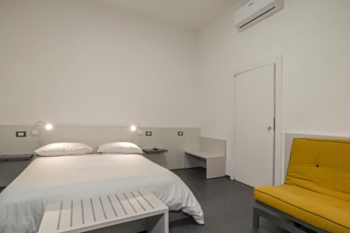 Camera da letto moderna di Casa Mirko ad Arezzo con letto bianco, divano giallo e design minimalista
