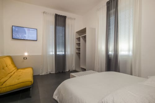 Camera moderna di Casa Mirko B&B ad Arezzo con sedia gialla, letto bianco e finestre a tutta altezza