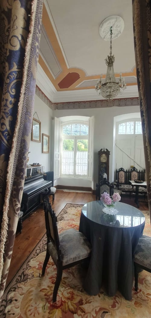 Elegante salón de La Venta de Miyares con techo ornamentado, araña de cristal, mesa redonda negra, piano y mobiliario de época