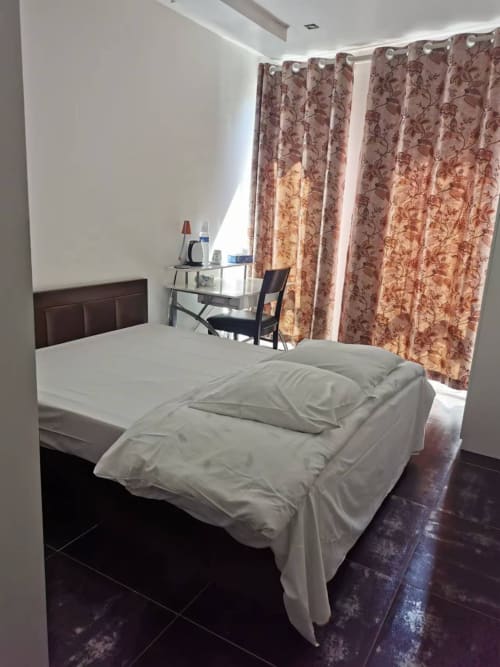 Chambre moderne à l'hôtel Chambre Pasteur à Montreuil avec literie blanche, rideaux fleuris et espace de travail avec WiFi