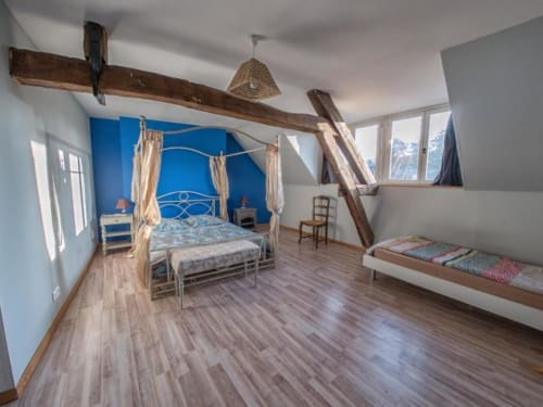 Chambre spacieuse au refuge des Alpes mancelles avec lit à baldaquin bleu, poutres en bois et vue sur les montagnes