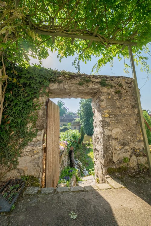 Entrée en arche de pierre avec porte en bois au refuge des Alpes mancelles à Fresnay-sur-Sarthe, pergola couverte de vignes au-dessus