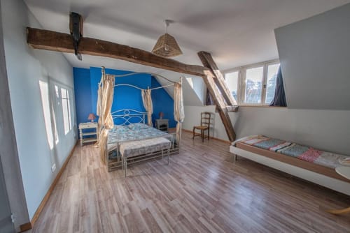 Chambre spacieuse au Refuge des Alpes mancelles avec mur d'accent bleu, lit à baldaquin, poutres en bois et vues sur les Alpes