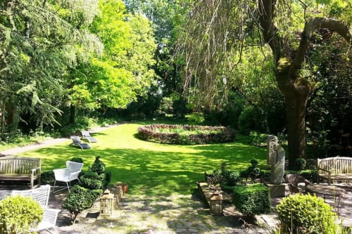 Serene garden at Le Grand Duc B&B in Valenciennes with lush lawn, mature trees, and comfortable seating areas