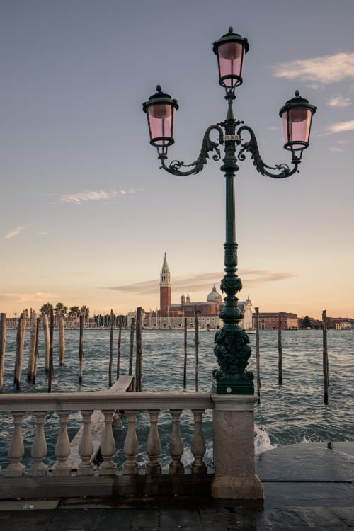 Ornate green street lamp with pink glass overlooking Venice's San Giorgio Maggiore church and Grand Canal mooring poles at
