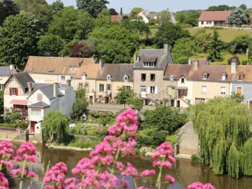 Charming riverside village with stone buildings and pink flowers in Fresnay-sur-Sarthe, France