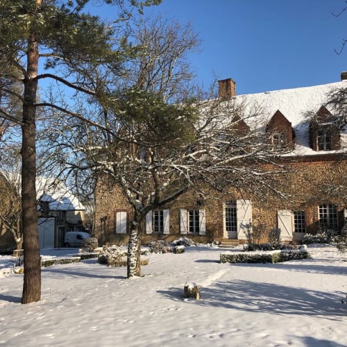 La cour enneigée du Prieuré Du Preux avec ses arbres nus et sa maison de ferme en brique, en hiver à Sépeaux Saint Romain