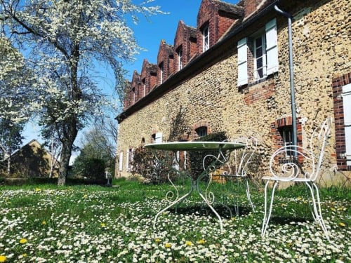 Garden seating at Le Prieuré Du Preux with white ornate chairs, flowering meadow, and historic stone building in Sépeaux