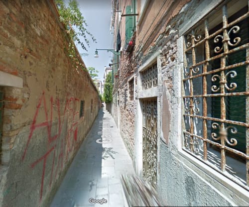 Narrow Venetian alley with historic stone buildings, ornate metal window grilles, and ivy-covered walls in Venice