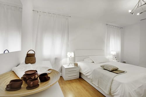 Bright minimalist bedroom in Venice apartment with white bed, wooden accents, sheer curtains, and tea service setup