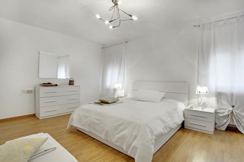 Modern white bedroom in Venice apartment with bed, dresser, nightstands, and wooden floors