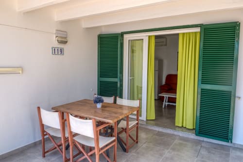 Patio del apartamento con vista al jardín en Las Golondrinas, mesa de comedor, contraventanas verdes y zona de estar