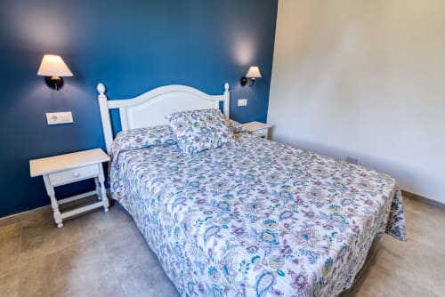 Dormitorio luminoso en Las Golondrinas con pared azul, cama blanca, sábanas florales, lámparas gemelas y piso de madera