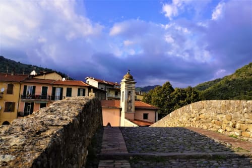 Sentiero in pietra che sovrasta il villaggio di Dolceacqua con edifici colorati, torre della chiesa e vedute montane presso l'Agritusmo Stecadò