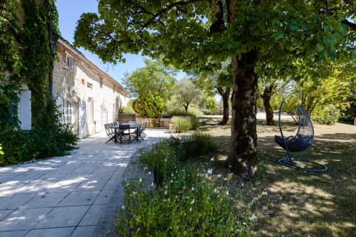 Ivy-covered cottage with patio seating and hanging chair at Les Lumieres Du Causse, surrounded by trees and green grounds in