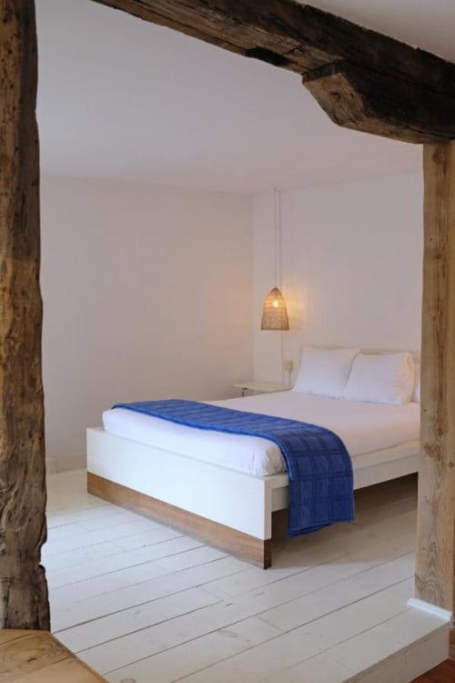 Dormitorio minimalista en Casa rural MAÑARINEGI con cama blanca, manta azul, vigas de madera, lámpara colgante y piso blanco