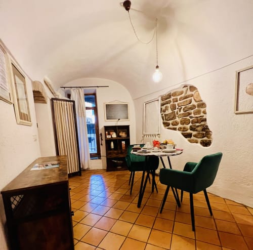 Salle à manger de l'appartement Casté à l'Agritourisme Stecadò de Dolceacqua avec chaises vertes, carrelage en terre cuite et mur en pierre apparente