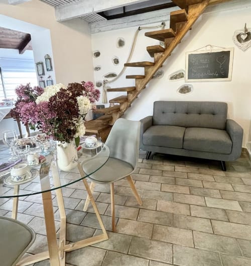 Séjour moderne avec canapé gris, table basse ronde en verre, fleurs fraîches, escalier en bois et murs blancs à l'Agritusmo Stecadò