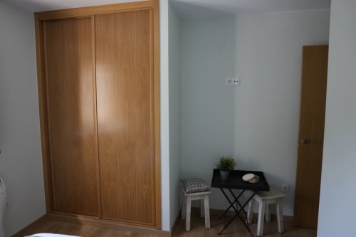 Dormitorio acogedor con armario de madera, mesita negra y taburetes blancos en Vivienda Balbino, León