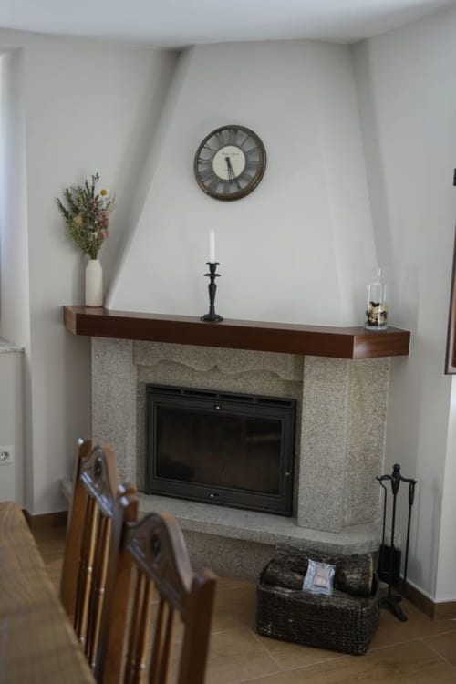 Chimenea moderna con repisa de madera, reloj y elementos decorativos en la casita Balbino, León