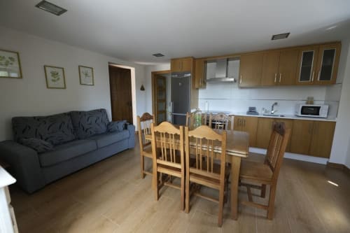 Sala de estar de cabaña abierta con mesa de comedor, sillas de madera, sofá azul y cocina en León, España