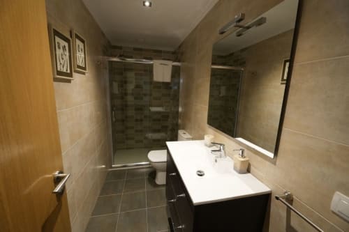 Cuarto de baño moderno en Vivienda de uso turístico Balbino, León con doble lavamanos, ducha y piso de azulejos oscuros