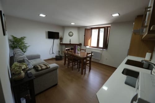 Área de estar de apartamento abierto con sofá gris, mesa de comedor, cocineta y TV de pared en alquiler vacacional Balbino