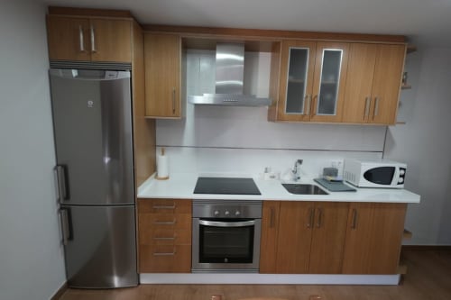 Cocina moderna con gabinetes de madera, electrodomésticos de acero inoxidable y encimera blanca en el alojamiento Balbino de León