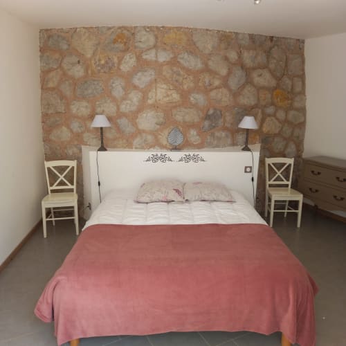 Chambre à la maison d'hôtes Sylvie CAMBON à Montséret avec mur en pierre, lit blanc, couvre-lit rose et vue sur le jardin