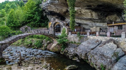 Hotel La Venta de Miyares ubicado bajo dramatica cueva acantilado, con arroyo, puente de piedra y rocas cubiertas de hiedra en Piloña, España