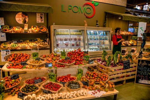 L Pomo market stand displaying fresh produce including tomatoes, peppers, garlic and baked goods in Bologna