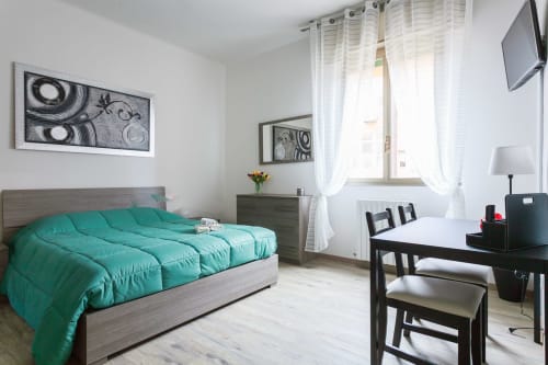 Camera moderna in appartamento bolognese con biancheria turchese, scrivania e balcone con tende bianche