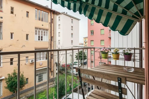 Bologna apartment balcony with green striped awning, potted flowers, metal railing, and colorful buildings