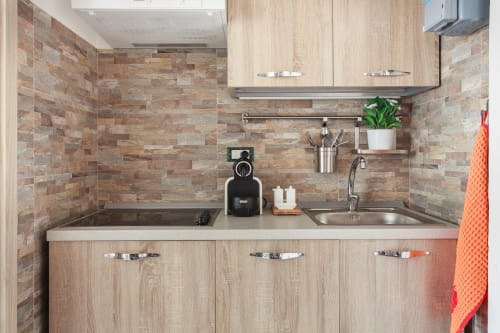 Modern kitchenette at L'Appartamento Giusto in Bologna with light wood cabinets, brick tile backsplash, and stainless steel