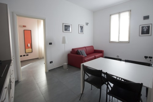 L'appartamento Nest a Bologna con zona living, tavolo da pranzo bianco, divano rosso e luce naturale dalle finestre