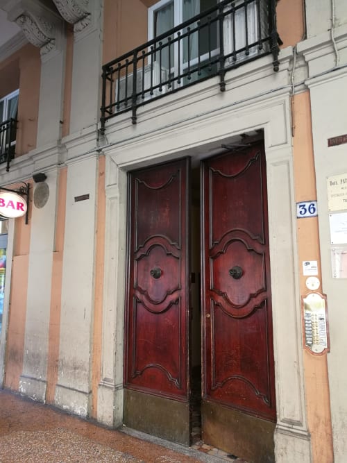 Storiche porte in legno rosso con pannelli decorati all'ingresso di L'Appartamento Giusto, facciata del palazzo residenziale a Bologna