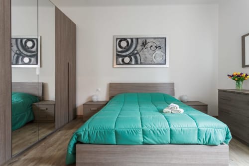 Modern bedroom at L'Appartamento Giusto in Bologna with turquoise comforter, wood furniture, and mirrored wardrobe