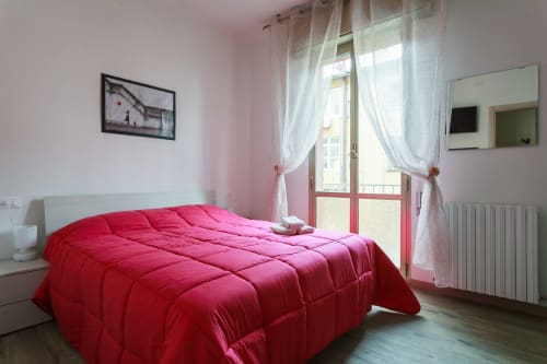 Bright bedroom in Bologna B&B Il Filo di Arianna with red quilted comforter, balcony doors, sheer curtains, and modern
