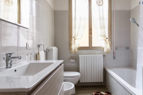 Modern bathroom at L'Appartamento Giusto in Bologna featuring white sink, toilet, radiator, and walk-in shower with natural