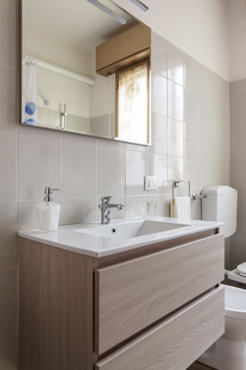 Modern bathroom in L'Appartamento Giusto Bologna with white tile walls, wooden vanity, mirror, and chrome fixtures