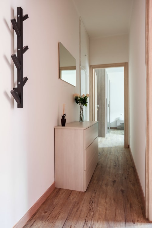 Modern hallway in Bologna B&B apartment with light wood flooring, pink walls, black coat rack, wooden dresser with mirror,