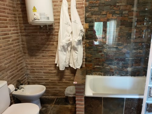 Baño de la cabaña El Paraje del Chef con paredes de ladrillo, lavabo, inodoro, ducha con mampara de vidrio y toallas blancas