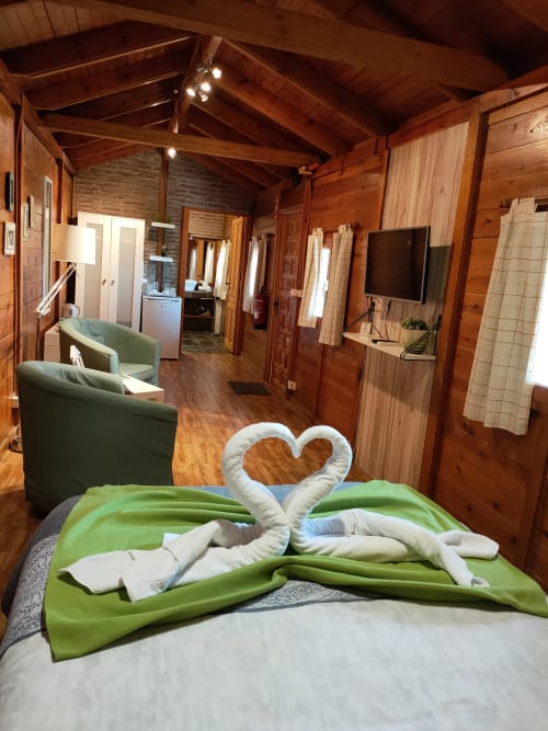 Acogedora habitación de cabaña con corazón de toalla blanca sobre ropa de cama verde, vigas de madera, chimenea y vistas a las montañas en El Paraje del