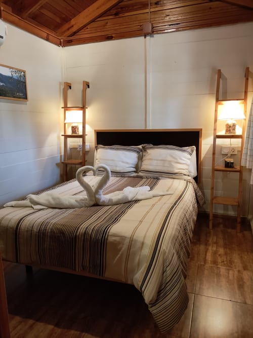 Acogedora habitación en la cabaña El Paraje del Chef en Laroles, Granada con ropa de cama rayada, cisnes de toalla y escalera de madera