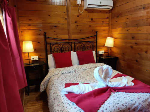 Acogedora habitación de cabaña rústica con cama de hierro forjado, detalles en rojo y vistas a la montaña en El Paraje del Chef
