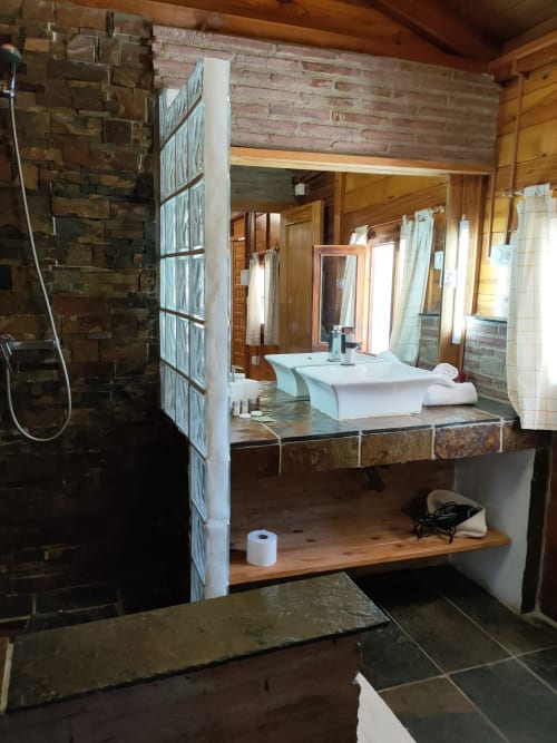 Cuarto de baño de lujo en Cabaña Amapola del Mulhacén en El Paraje del Chef, con paredes de piedra, lavabo blanco moderno y vistas a la montaña